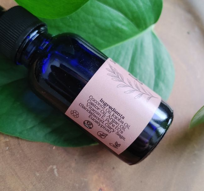 Beard oil bottle with black cap, pink back label with ingredient text.