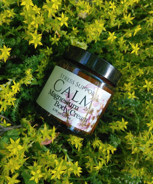 Magnesium body cream jar with black lid on green foliage, pink flower on label