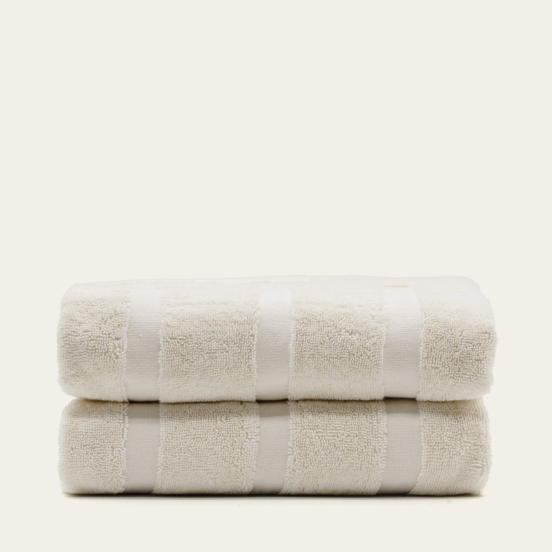 Two folded cotton towels in off-white with wide stripe band across the middle.