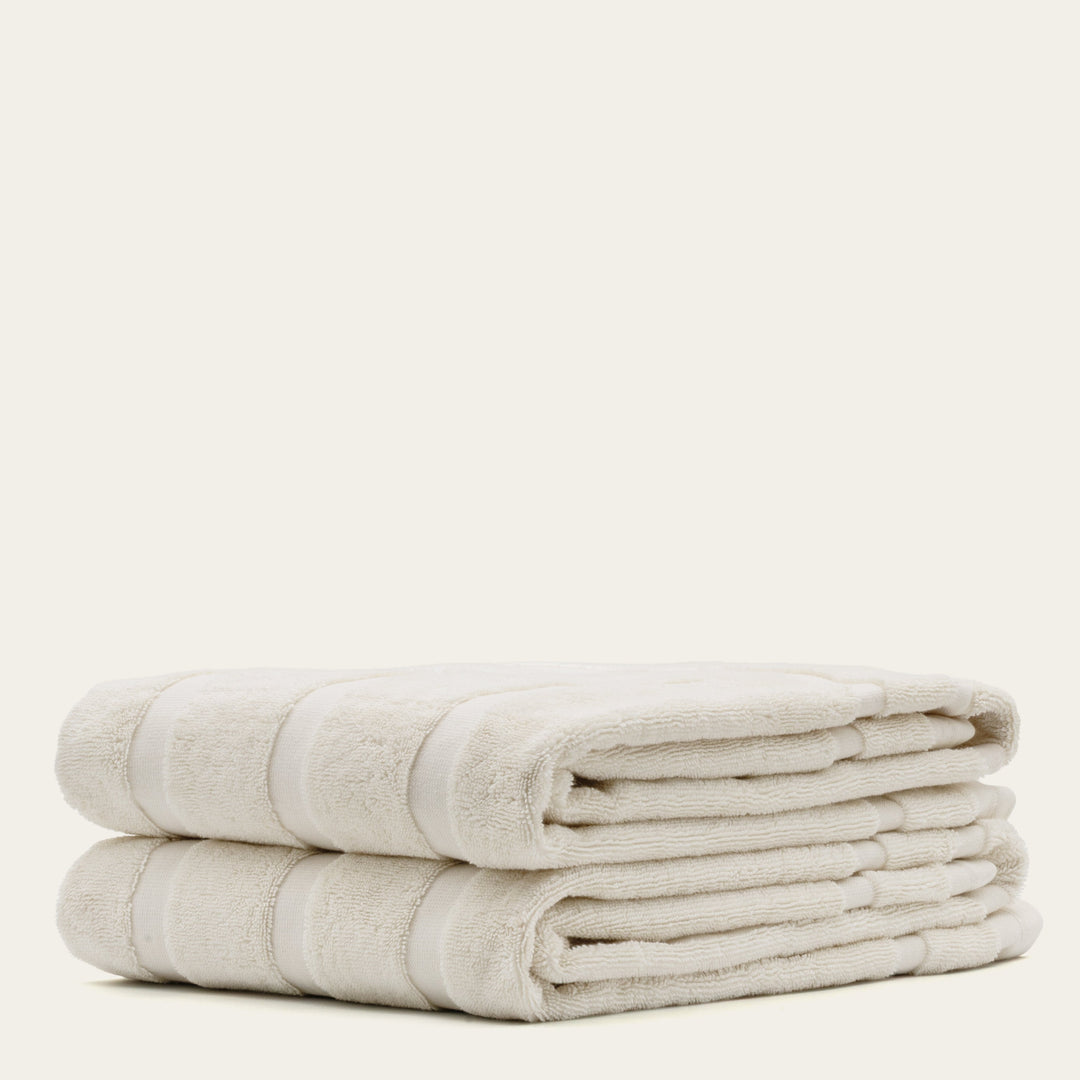 Two rolled cotton towels in off-white with subtle stripe bands.