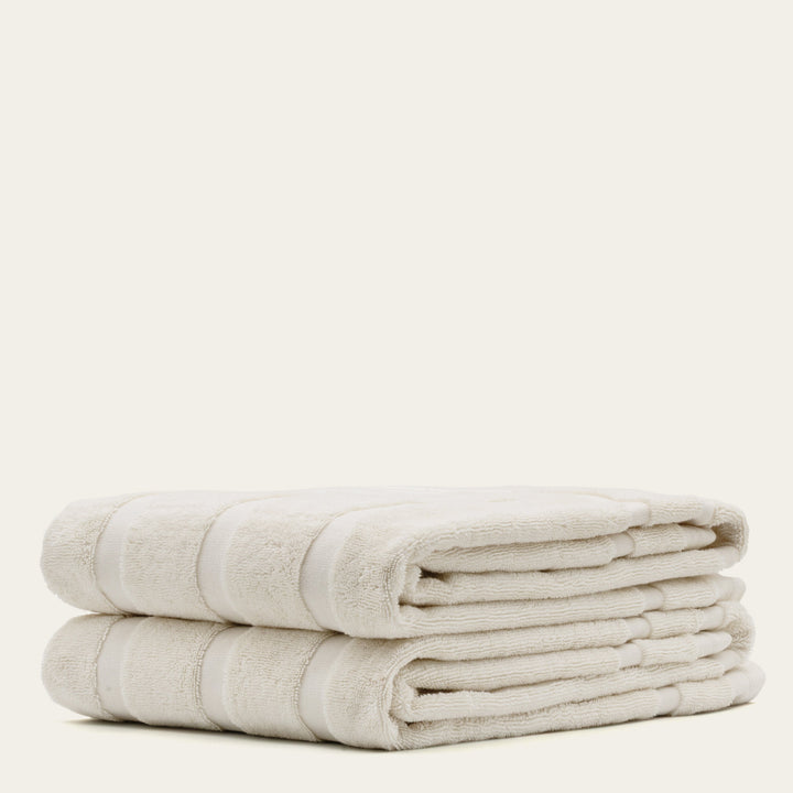 Two rolled cotton towels in off-white with subtle stripe bands.