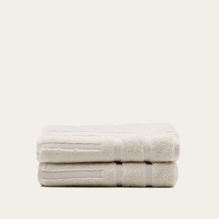 Folded cotton towels in light beige with embroidered-style border strip detail