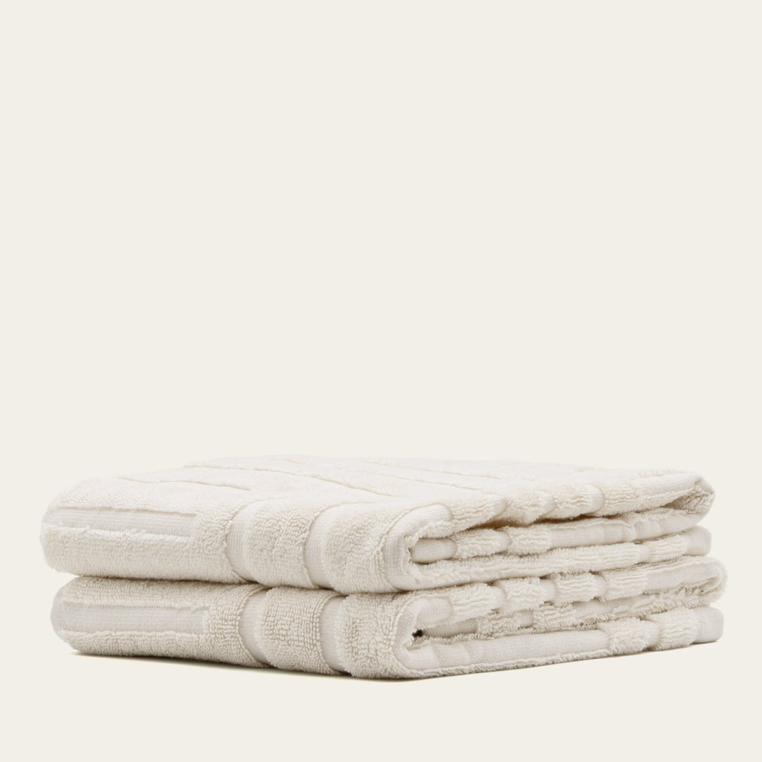 Folded ecru cotton towels with layered edges and stripe detail
