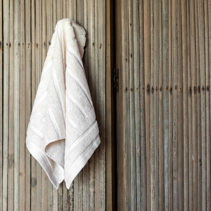White hand towel hanging with decorative stitched border and textured woven surface