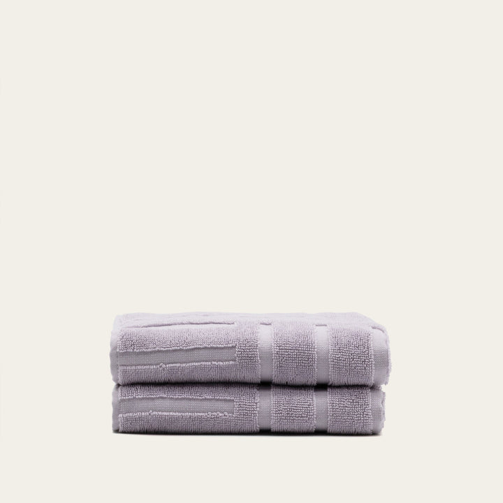 Lilac terry bath towels folded together with coordinated horizontal and vertical border stripes.