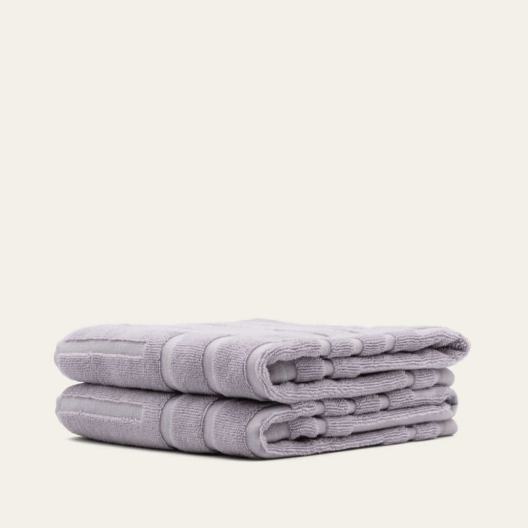 Lilac terry towels stacked with a folded edge detail and thick, absorbent weave.