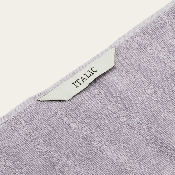 Lilac towel corner with fabric tag reading “ITALIC” and textured loop weave