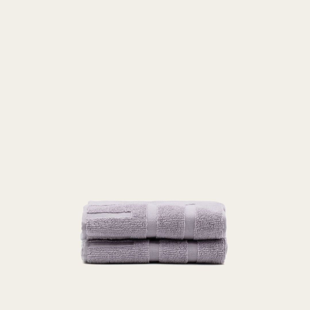 Lilac terry bath towels, folded in a stack with matching striped borders.