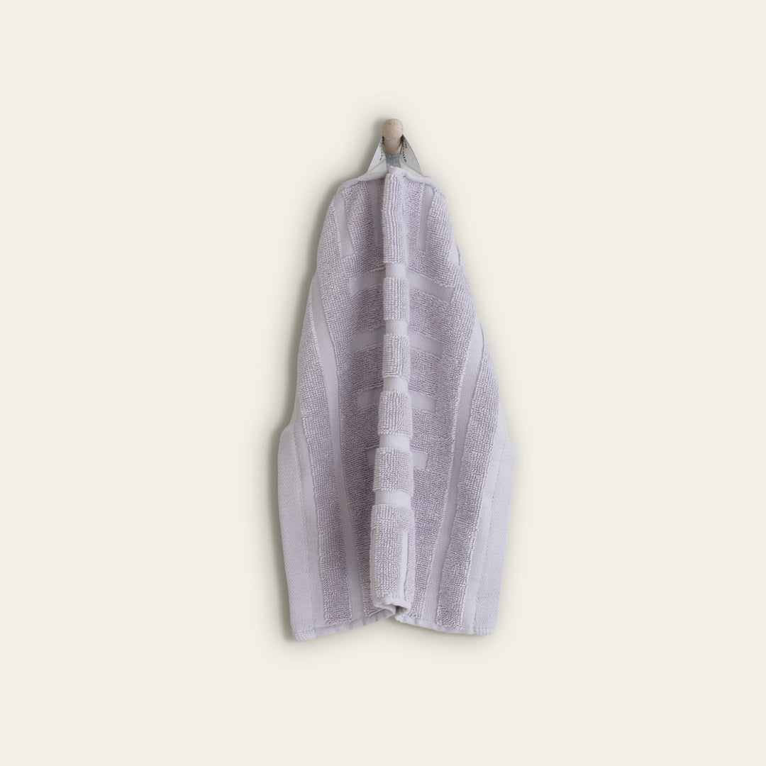 Lilac hand towel folded and hanging, with looped terry texture and center stripe detail.