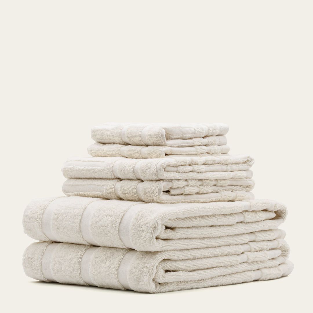 Stack of folded cotton towels in off-white with subtle stripe bands.