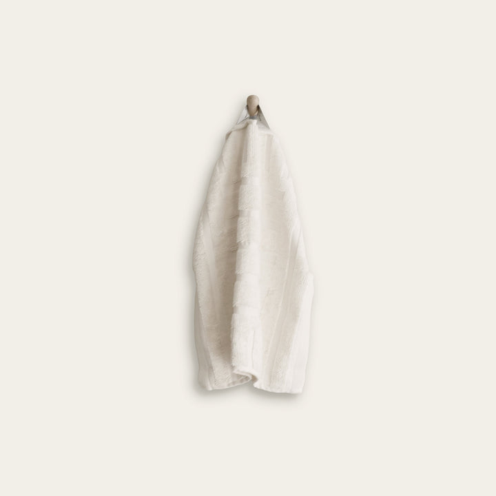 Ecru cotton hand towel hanging by loop, folded terry with subtle patterned trim