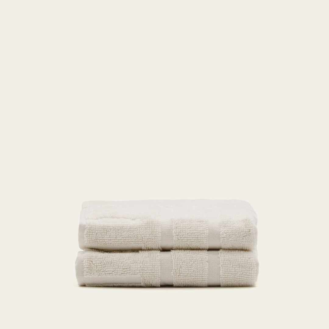 Two folded light beige cotton towels with stitched band detail and terry texture