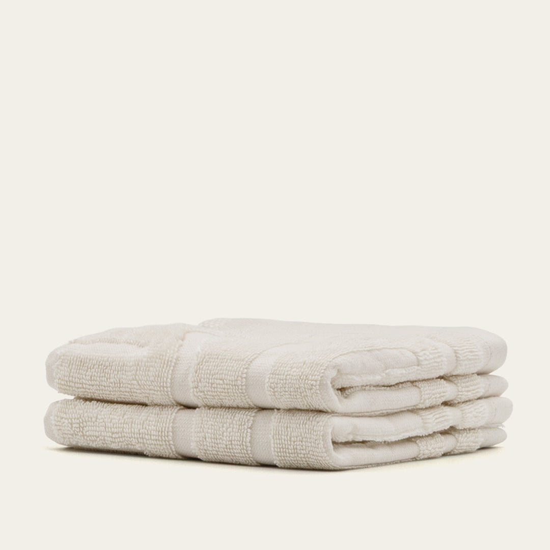 Stacked light beige cotton towels, folded with stitched bands and soft terry loops
