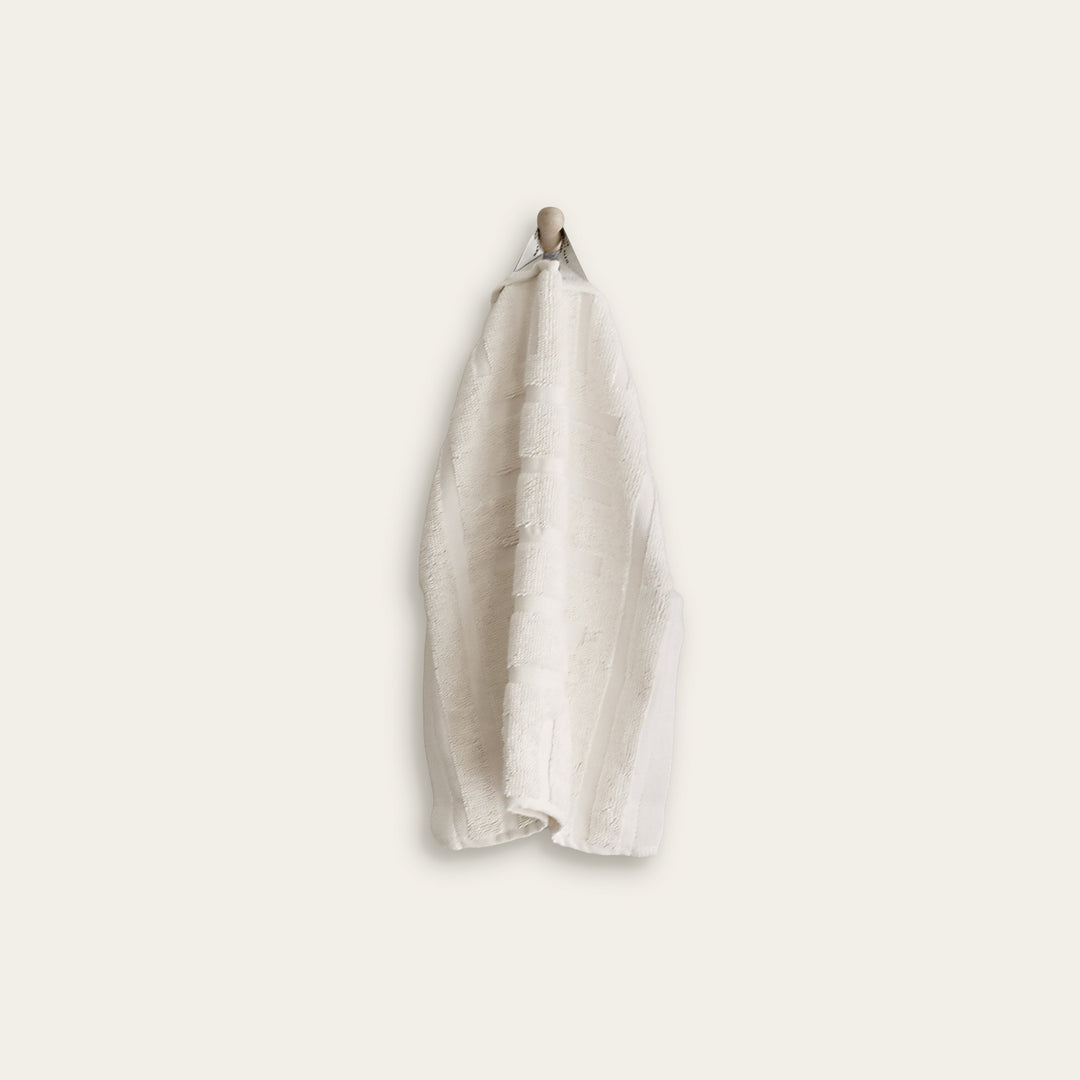 Cotton hand towel hanging from a metal hook, off-white with subtle woven texture