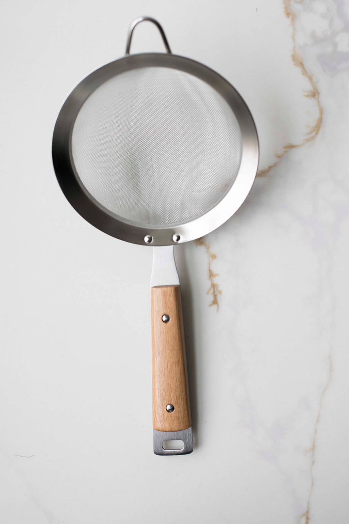 Round mesh strainer with dark metal rim, wood handle with hanging loop