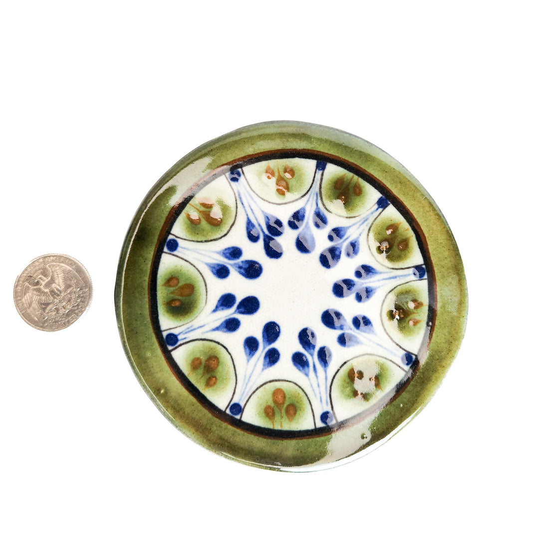 Round ceramic coaster with white, blue, and green leaf pattern; coin for scale.
