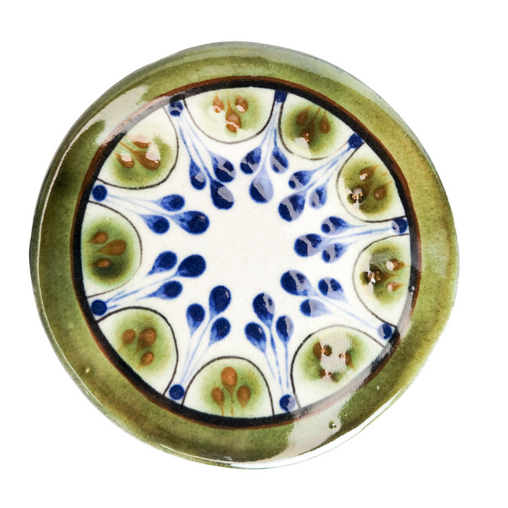 Round ceramic coaster, white center with blue drips and green leaf accents.