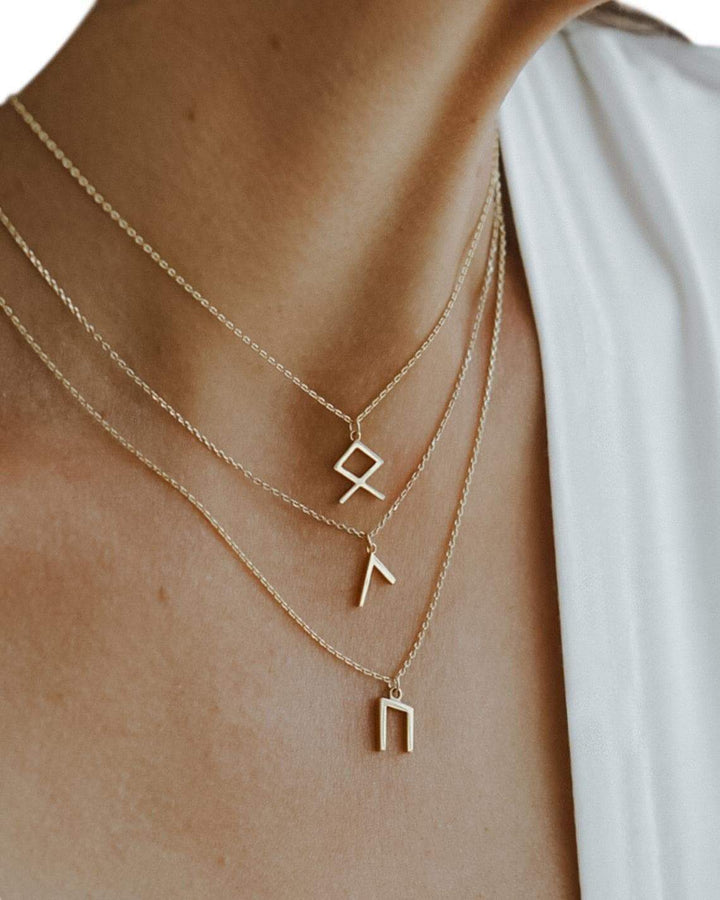 Gold-tone rune pendant necklace on skin with layered chain and small symbol charms