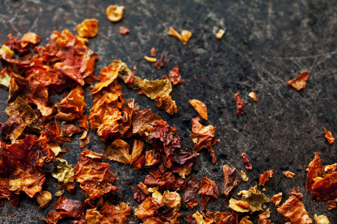 Ghost chile flake seasoning, small red-orange dried chili flakes on a dark surface
