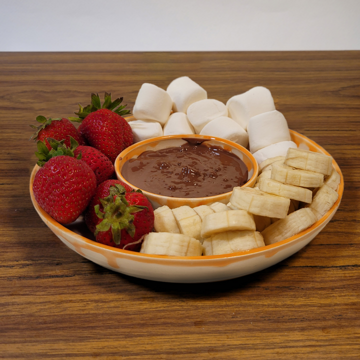 Ceramic dip platter holding chocolate dip with strawberries and banana pieces