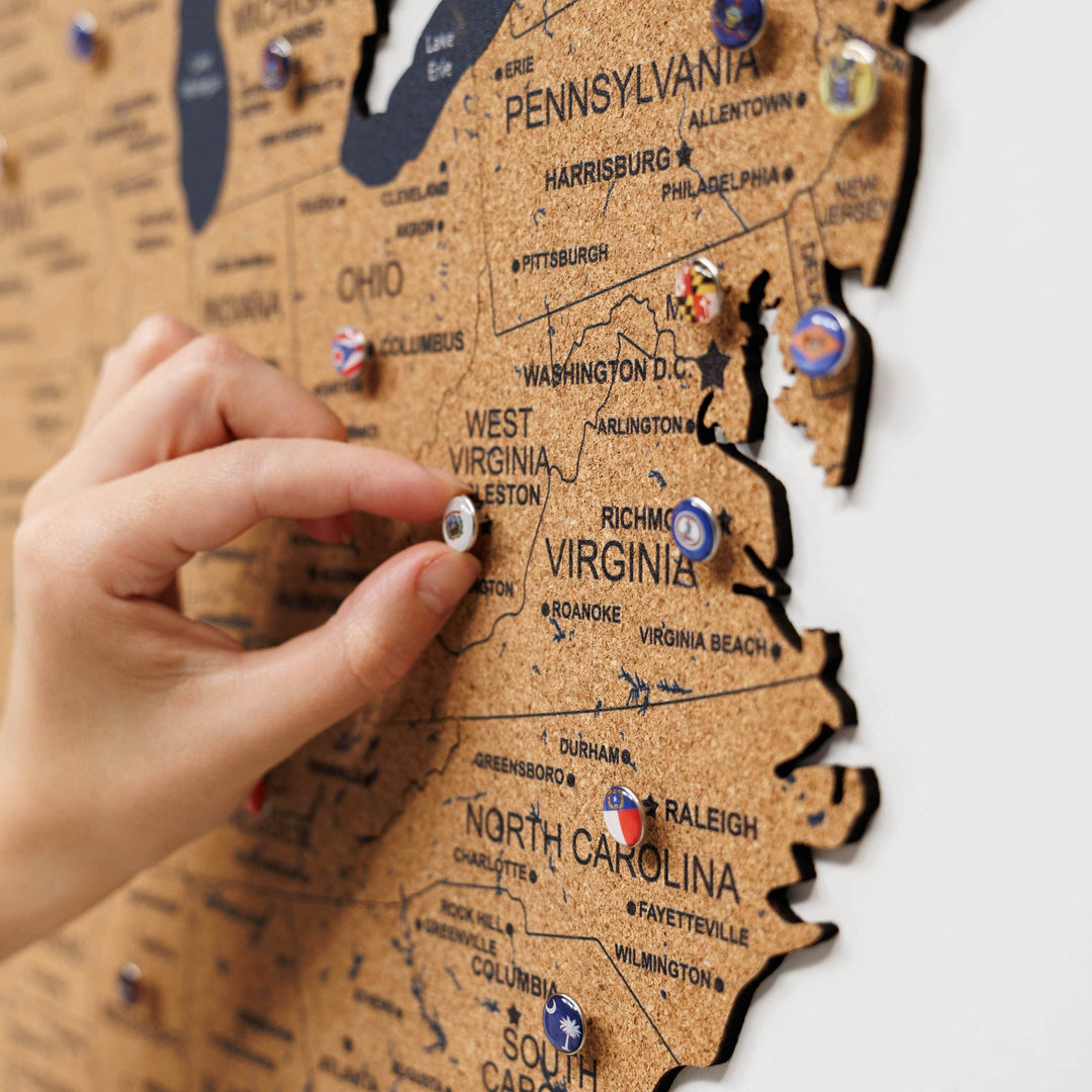Close-up of hands placing a push pin on a cork USA map board