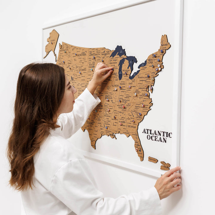 Woman placing push pins on a framed cork USA map on a wall