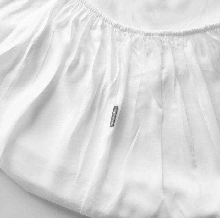 White fitted crib mattress protector with elastic bed skirt and sewn label