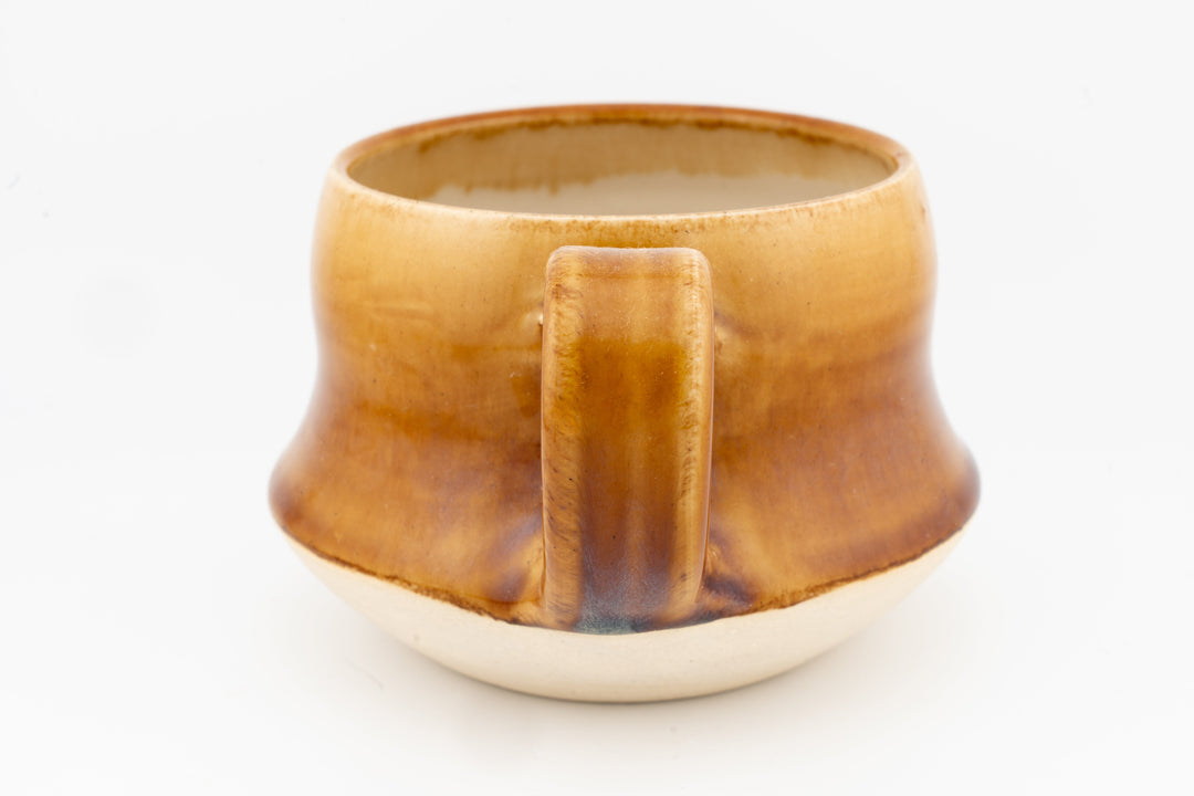 Wide ceramic mug with amber-gold glaze and front center handle detail, speckled rim