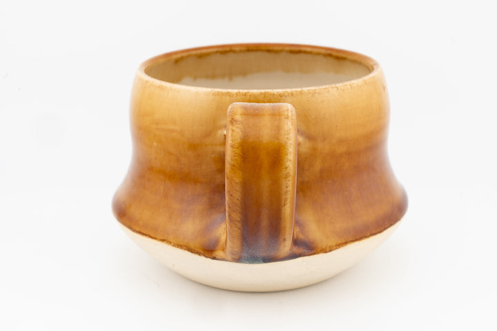 Wide ceramic mug with amber-gold glaze and front center handle detail, speckled rim