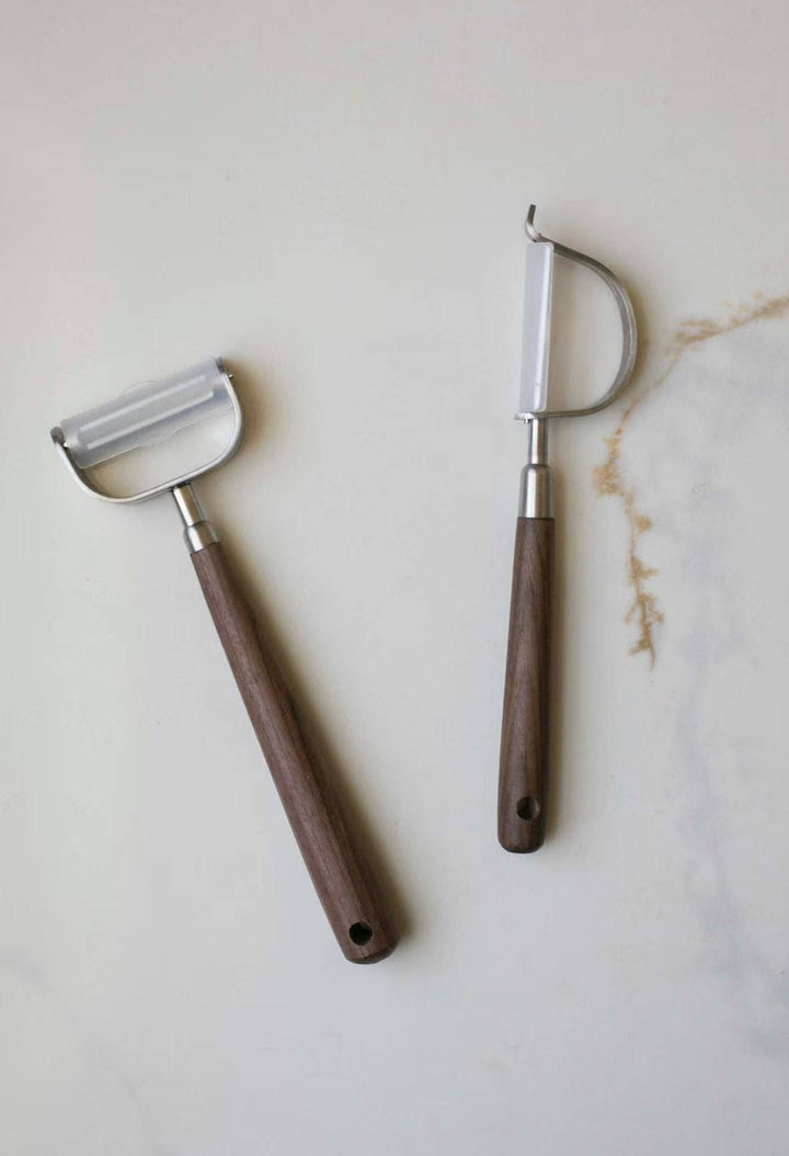 Two vegetable peelers with curved stainless blades and brown wooden handles
