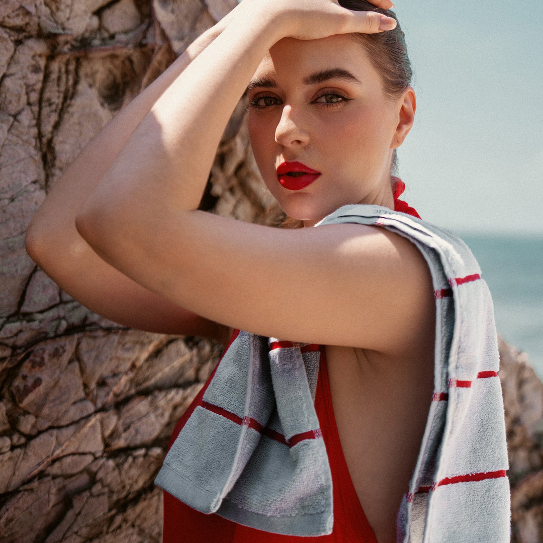 Gray cotton towel with red stripes held over shoulder by a woman outdoors.