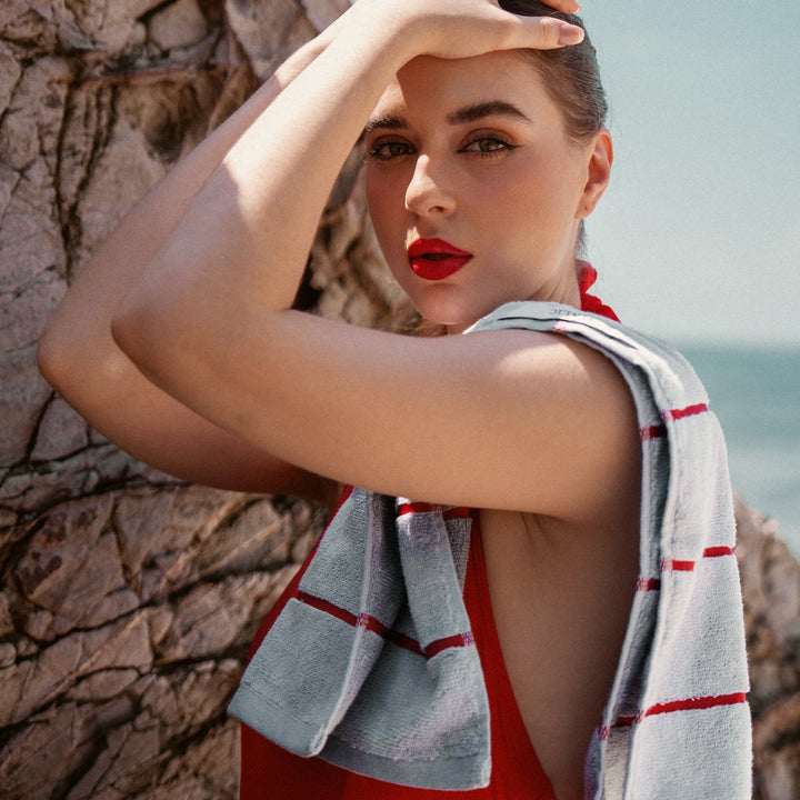 Gray cotton towel with red stripes held over shoulder by a woman outdoors.