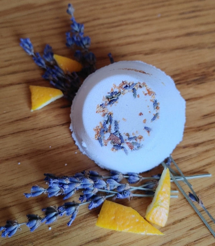 Round white shower steamer with dried lavender and citrus pieces on a wooden surface