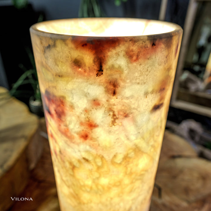 Onyx table lamp close-up: lit cylindrical shade with amber and speckled veining