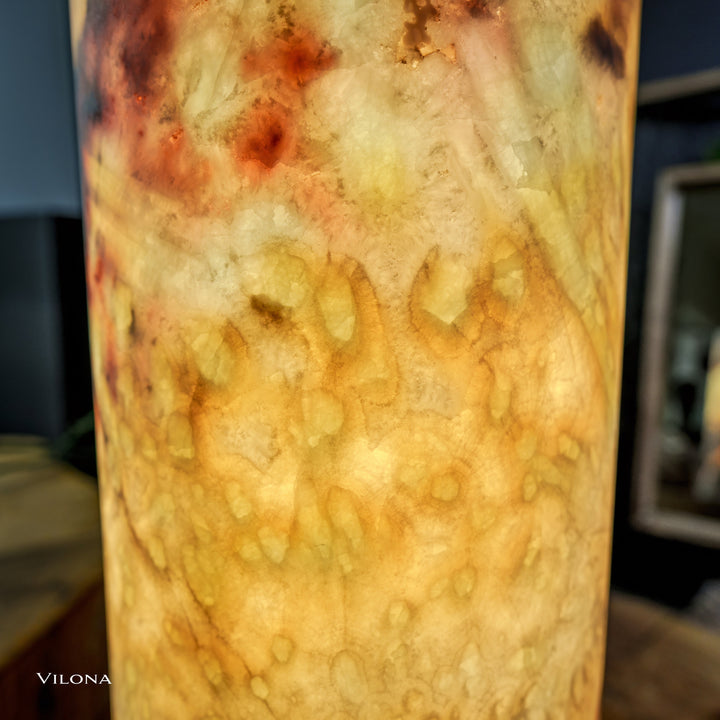 Onyx table lamp close-up: glowing cylindrical shade with pale amber and dark flecks