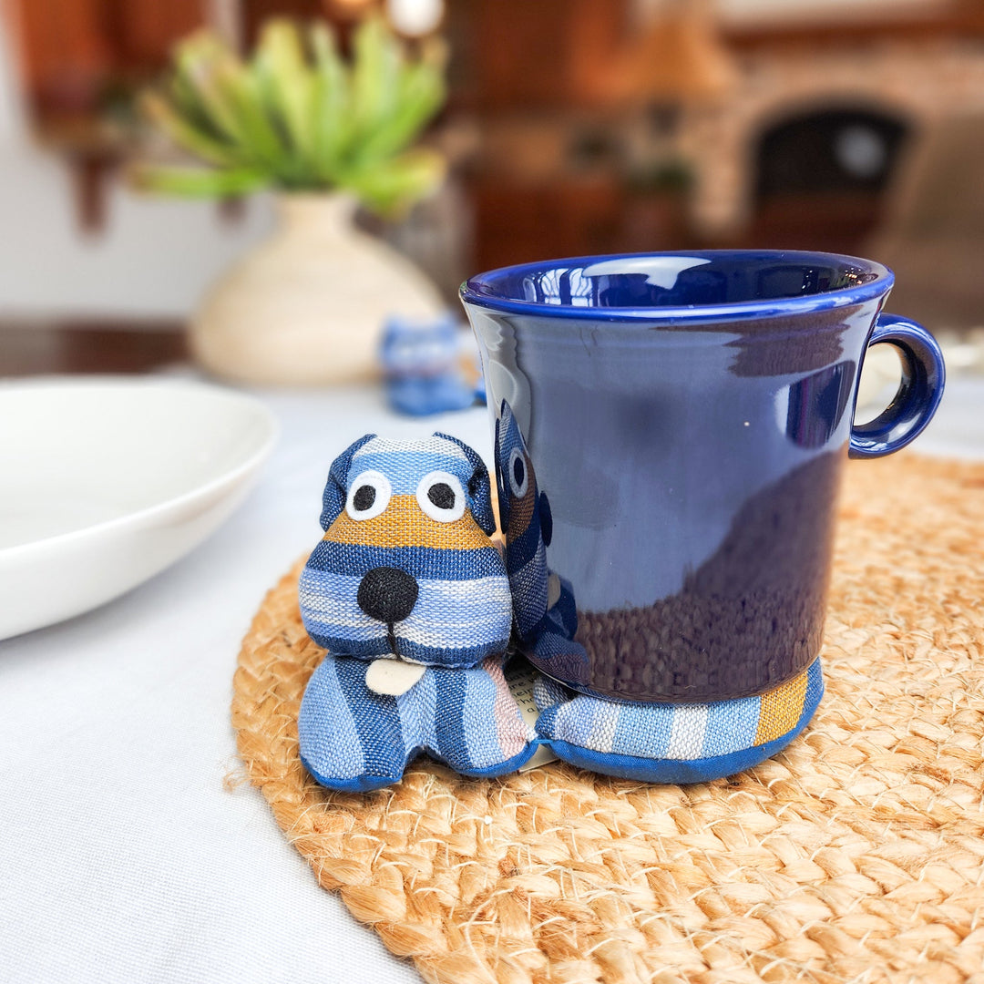 Round woven trivet with blue striped dog next to a glossy blue ceramic mug