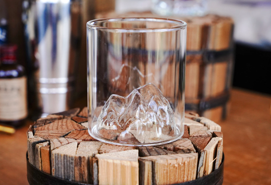 Clear whiskey tumbler with ice cubes and mountain range etched design on glass