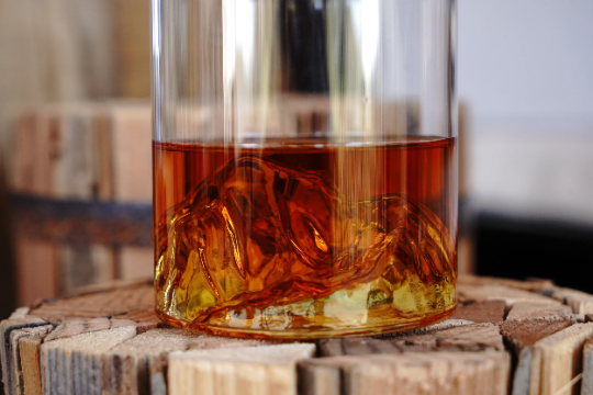 Whiskey-filled clear tumbler with ice and mountain range etched detail