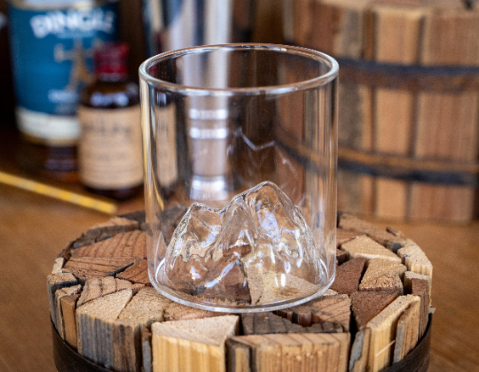 Clear whiskey tumbler with ice cubes and mountain range etched detail on the front