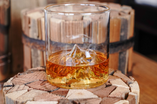 Clear whiskey glass filled with amber whiskey and ice, mountain range etching visible