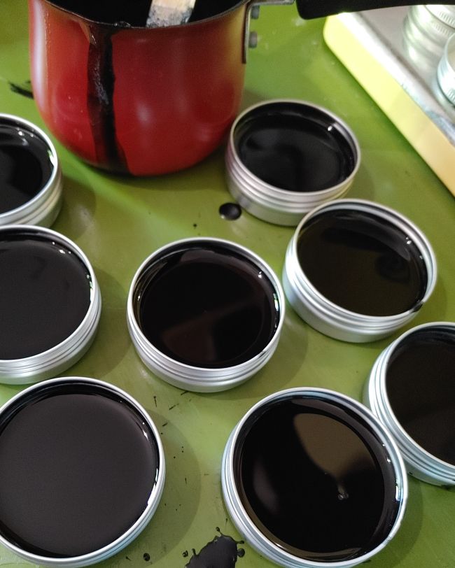 Assorted drawing salve tins with dark balm, open lids on a surface