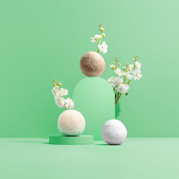Wool dryer balls with flowers and a wooden laundry scoop on a pedestal