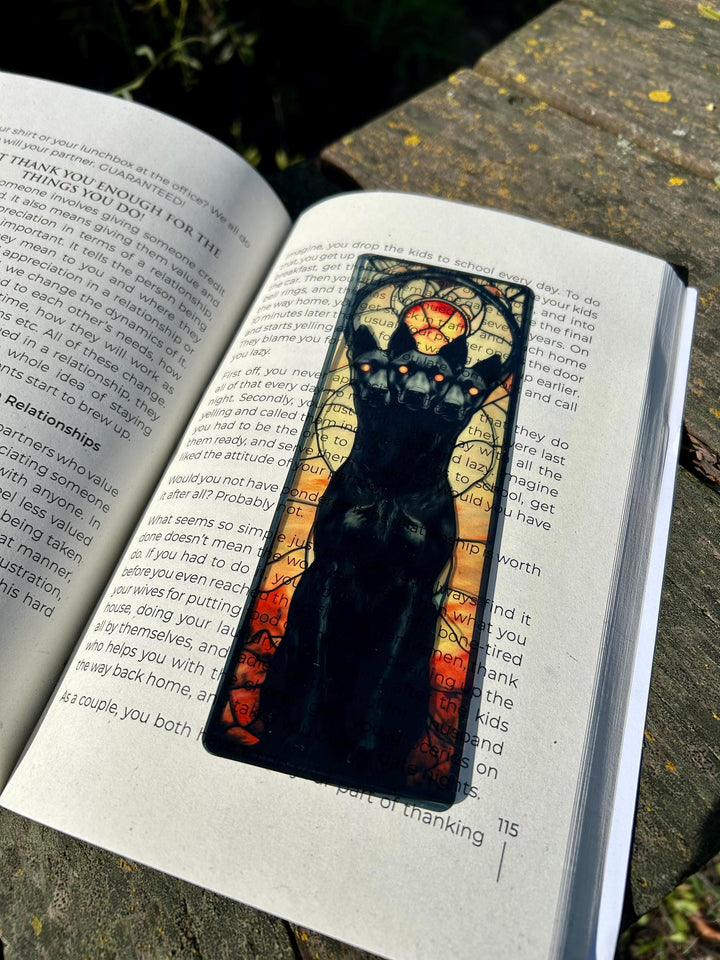Fantasy bookmark showing black three-headed dog face with blue halo on open book page