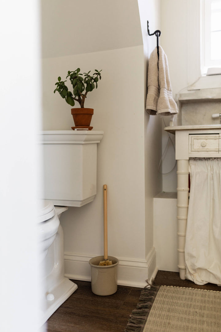 Toilet brush with wood handle in beige holder near toilet