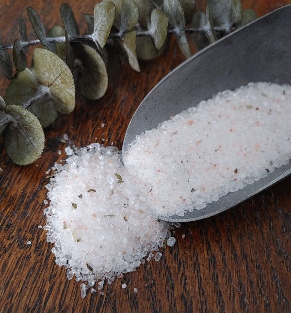 Spoon of bath salt crystals with scattered dried leaves on wooden surface