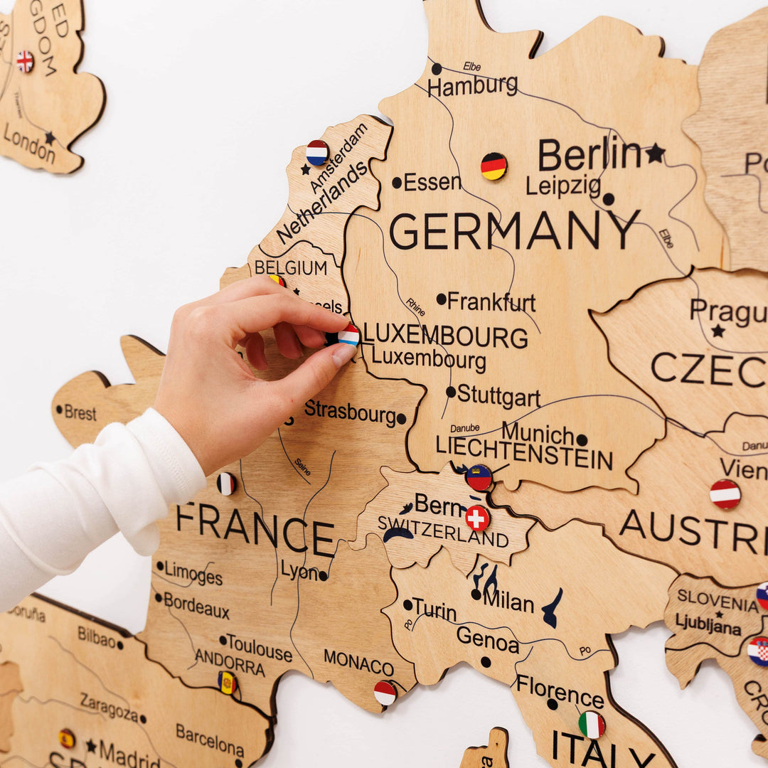 Wooden Europe map close-up with raised regions and country labels; hand presses