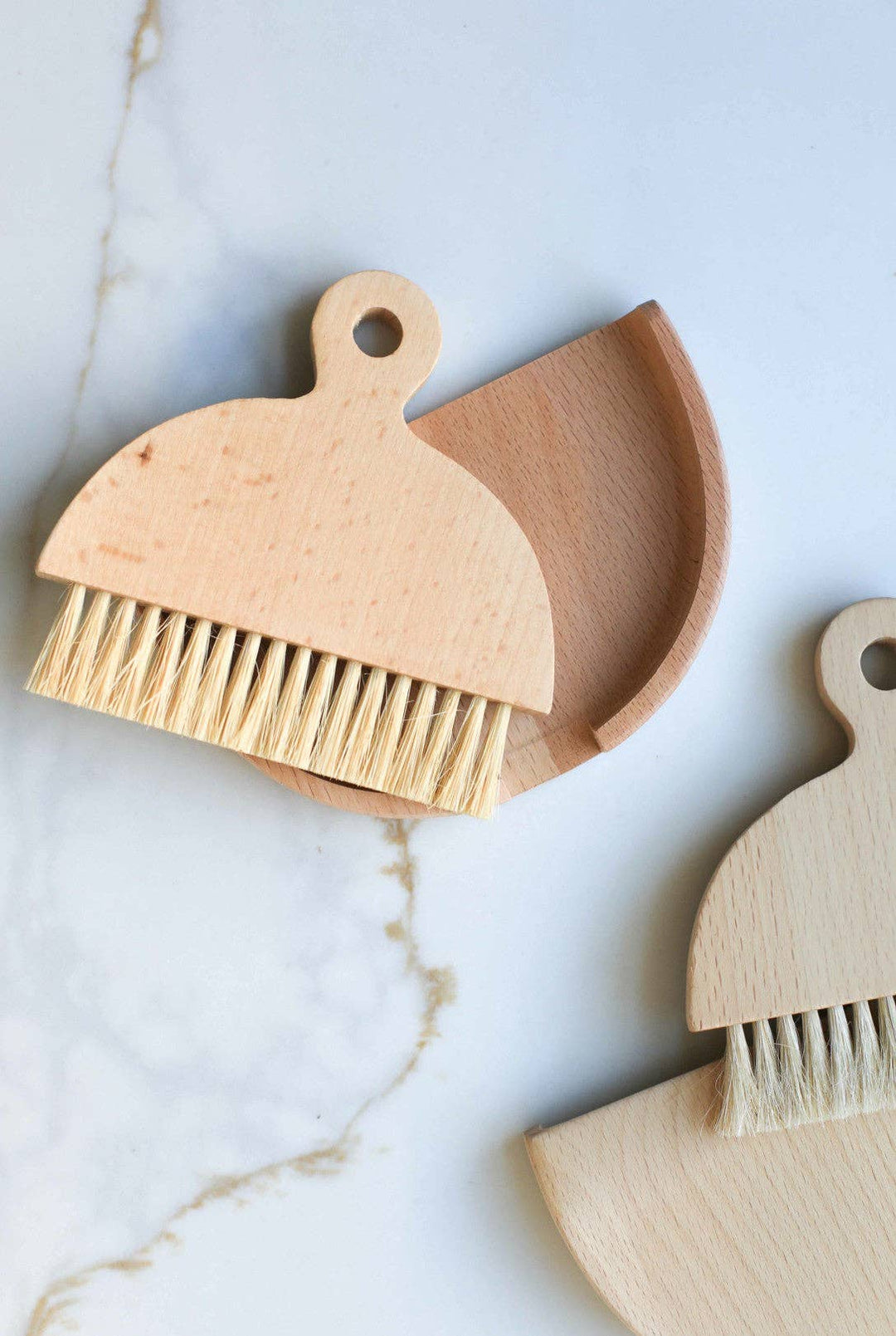Wooden table brush with rounded body, loop handle, tan bristles, angled view