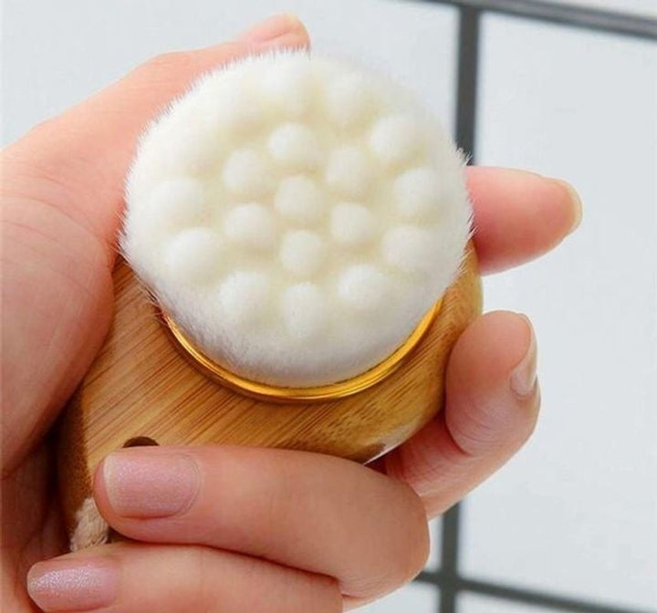 Close-up of bamboo facial brush with dense white bristle head in hand