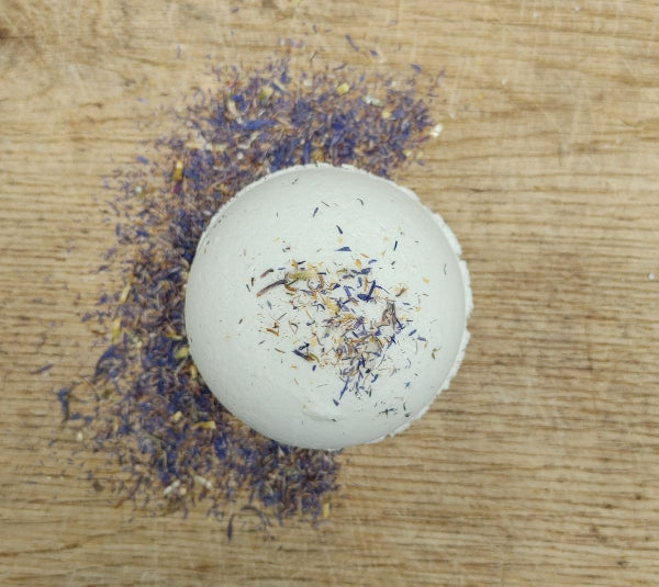 Round white bath bomb with scattered lavender-like dried flakes on surface