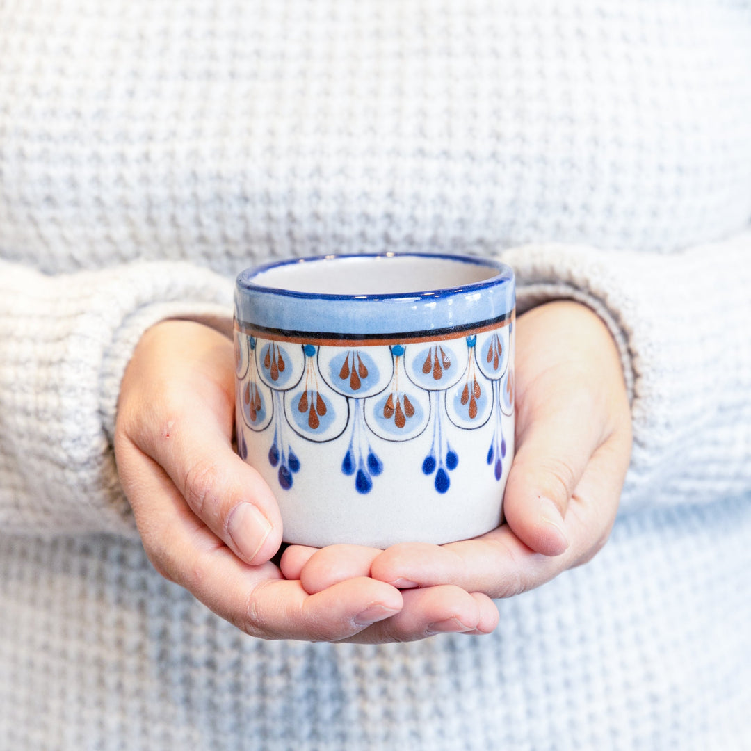 Stoneware cup with amber liquid inside, blue and orange raindrop motif, glossy blue rim.